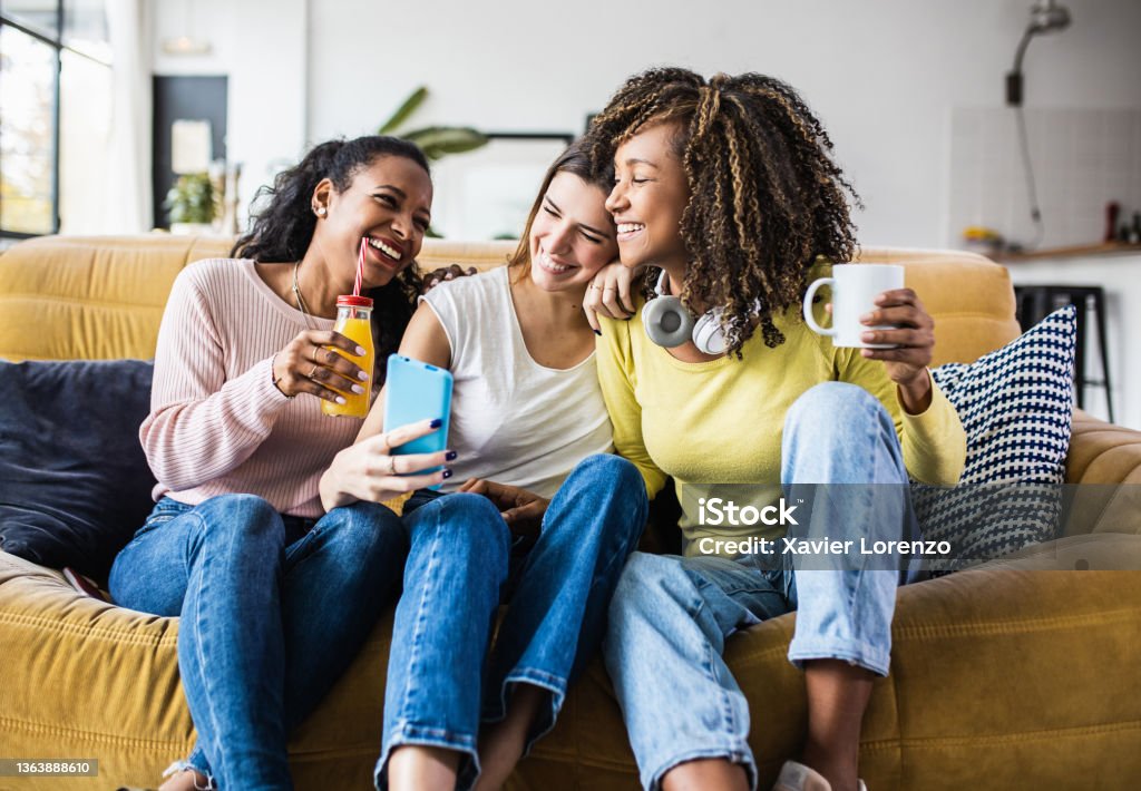 Cheerful multiracial female friends enjoying free time together at home Cheerful multiracial female friends enjoying free time together at home - Three happy young adult women hanging out while - Friendship and social gathering concept Friendship Stock Photo