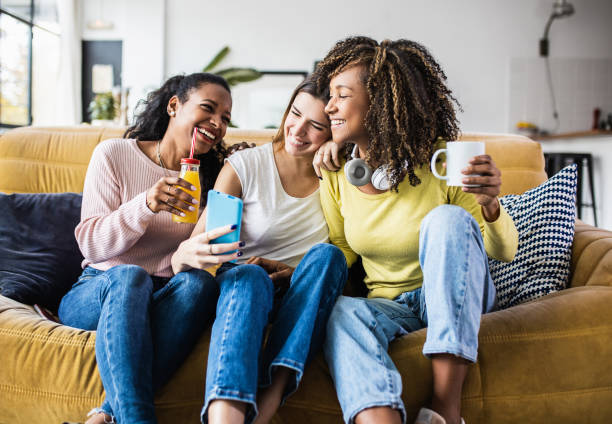 Cheerful multiracial female friends enjoying free time together at home Cheerful multiracial female friends enjoying free time together at home - Three happy young adult women hanging out while - Friendship and social gathering concept friends laughing stock pictures, royalty-free photos & images