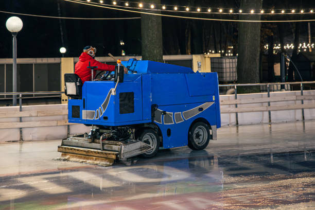 A stadium worker cleans an ice rink on a blue modern ice cleaning machine.