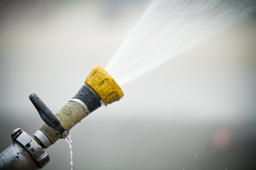Fixed fire hose spraying water with blurred background.