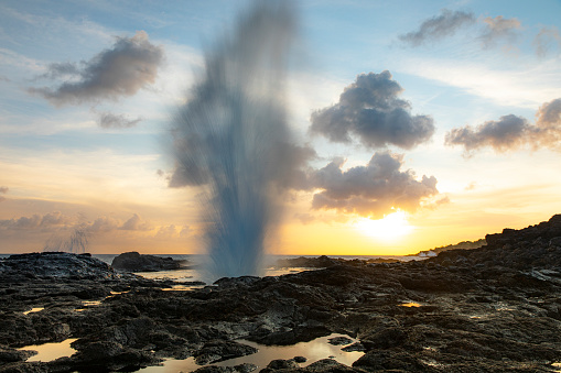 Slow shutter of water geyser shooting into sky at sunset in on Hawaiian rocky coast