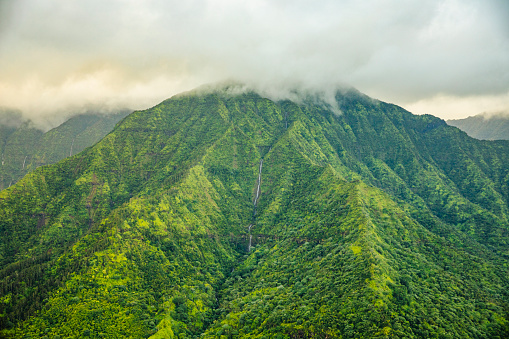 Clouds hovering above lush green mountain range in Hawaii