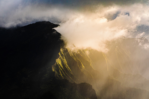 Golden light shining through clouds along the side of Hawaiian mountain peak