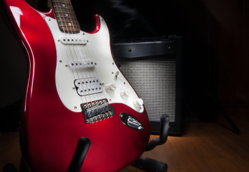red and white electric guitar and combo amplifier on black background