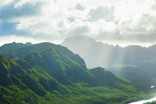 Clouds hovering above lush green hawaiian mountain range in golden sunset light