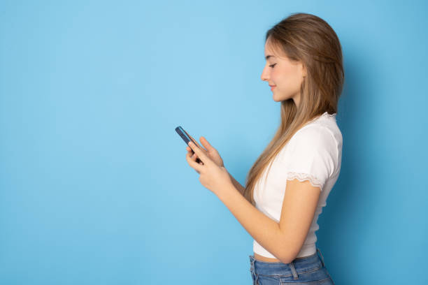 istock Beautiful girl using smartphone standing isolated over blue background. 1363892753