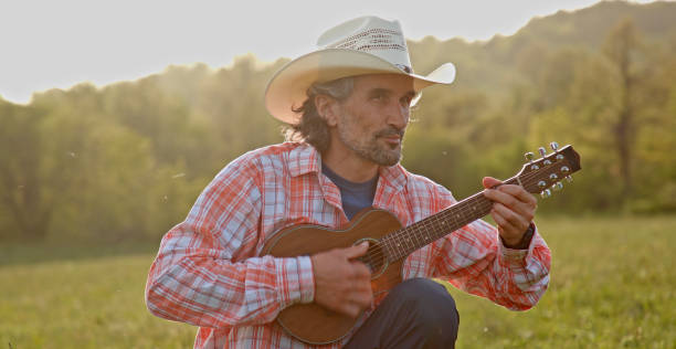 istock Cowboy in nature playing the guitar at sunset. Springtime stayca 1363894304