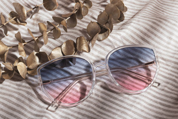 istock Transparent frame gradient sunglasses and golden eucalyptus are on gray striped cotton fabric 1363894345