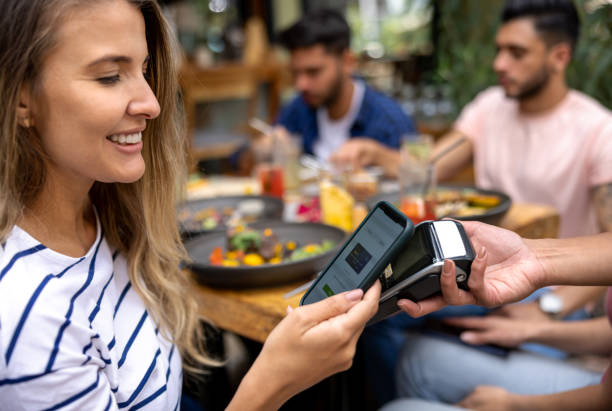 Woman making a contactless payment with her cell phone at a restaurant stock photo