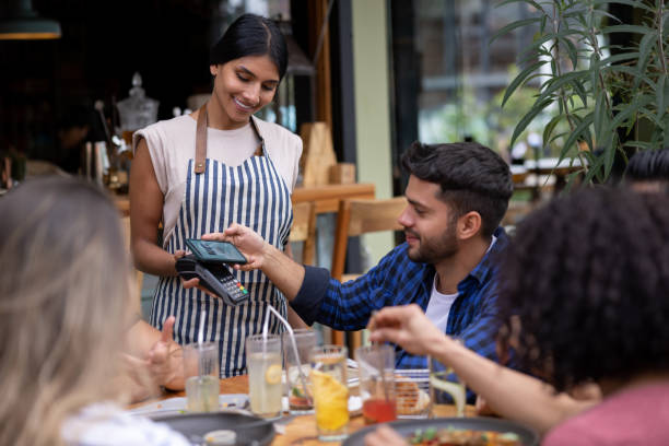 Man making a contactless payment with his phone at a restaurant Latin American man making a contactless payment with his phone to the waitress at a restaurant friends in bar with phones stock pictures, royalty-free photos & images