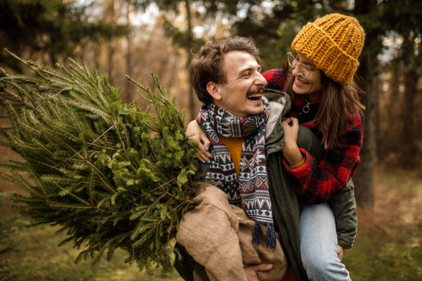 istock Young boy carrying her girlfriend on his back while carrying their new Christmas tree home 1363903990
