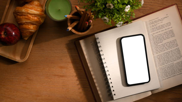 istock Worktable with smartphone mockup on a book on wooden table. 1363927352