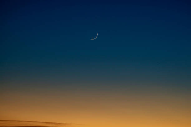 Waxing crescent moon shining in a twilight sky over a dark hillside