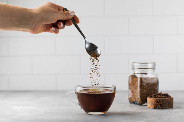 Woman stirs instant coffee in glass mug with boiled water on grey stone table Woman stirs instant granulated coffee in glass mug with hot boiled water by spoon on grey stone table in light kitchen closeup glass cup of boiling water stock pictures, royalty-free photos & images