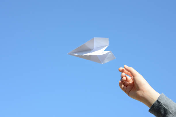 istock Child's hand and paper airplane on blue sky background 1363935806