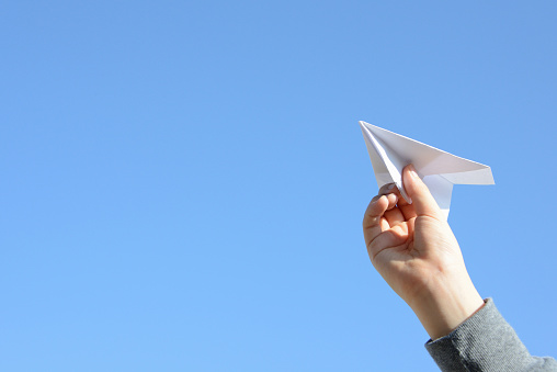 Child's hand and paper airplane on blue sky background