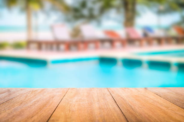 Wooden table with the swimming pool blurred background Image of wood table in front of a swimming pool blurred background. Brown wooden desk empty counter in front of the poolside on beautiful beach resort and outdoor spa. pond stock pictures, royalty-free photos & images