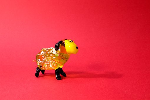 Miniature glass yellow lamb or sheep figurine on red background close up