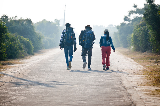 Rear view of young couple with backpack walking on road towards forest