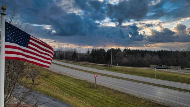 istock US flag moves in the wind under dramatic clouds next to road 1363945393