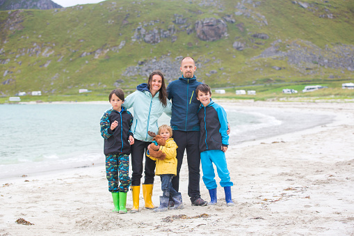 Happy family, enjoying white sand beaches in Lofoten, Norway on a summer cold rainy day, family concept