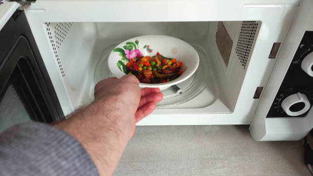 istock A man puts his hand a white bowl with a pattern with food in the microwave front view 1363952657