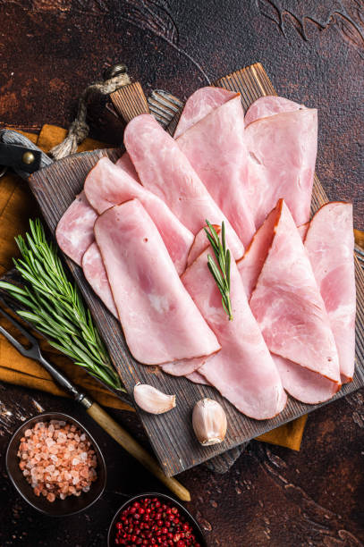 Flat slices of square sandwich ham with herbs. Dark background. Top view