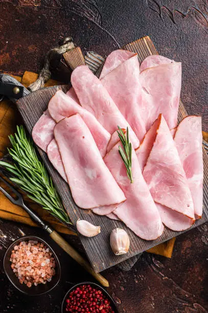 Flat slices of square sandwich ham with herbs. Dark background. Top view.