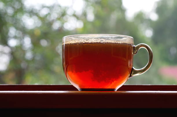 There is a glass mug with tea on the windowsill of an open window