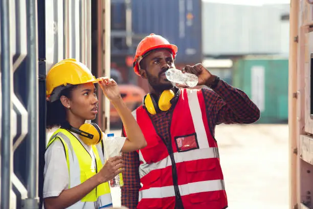 Photo of Man and woman american african technician drinking water and resting after working at container yard.