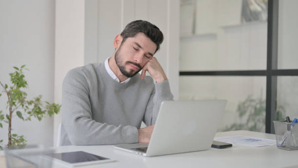 istock Tired Young Man taking Nap While Sitting in Office with Laptop 1363972958