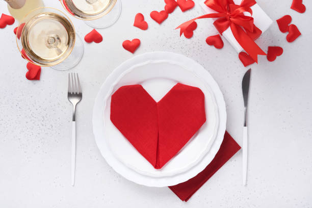 istock Valentinas day table setting white color with white silverware, red napkin folded as heart, candles, champagne, glasses on white background for greetings. Romantic dinner or menu concept. Mock up. 1363973433