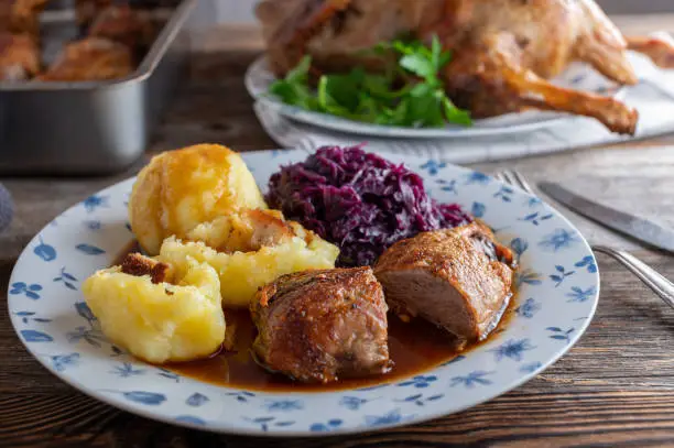 Traditional german holiday meal with roasted duck, potato dumplings, red cabbage and a delicious gravy. Homemade cooked and served on rustic and wooden table.