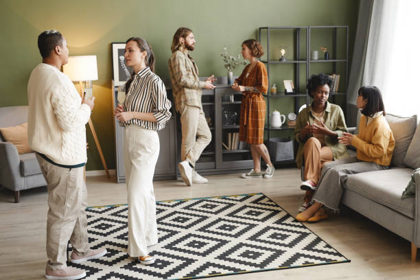 Group of young people talking to each other and drinking wine during home party in the living room