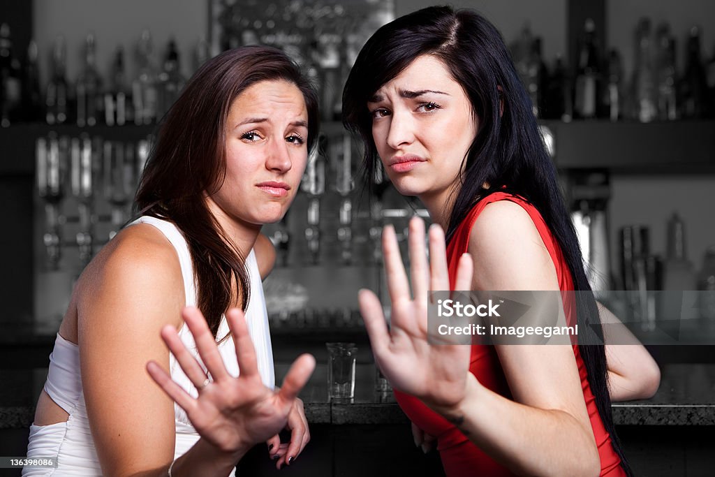 Two women with disgusted faces holding up their palms Two young women at a bar who don`t want to be harassed. Sexual Harassment Stock Photo