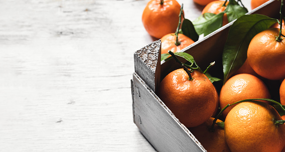 A box with fresh tangerines on on a white wooden table with copy space