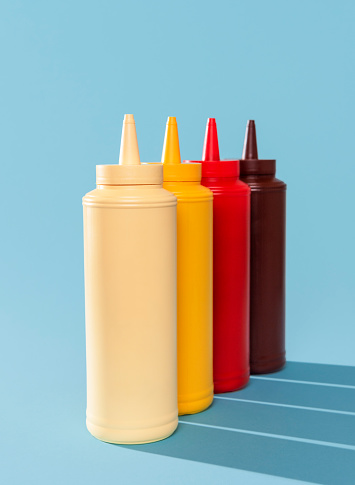 Close-up with multiple sauce bottles on a blue table. Variety of sauce in plastic bottles isolated on a blue background.
