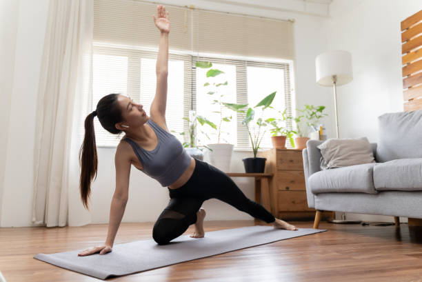 Beautiful young woman practicing yoga at home Portrait of Beautiful young Asian woman practicing yoga in living room. Young healthy girl doing yoga stretching at home YOGA stock pictures, royalty-free photos & images