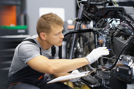 A man in the garage is checking a motorcycle, close-up. Wear test of parts, engine and suspension. Service station specialist
