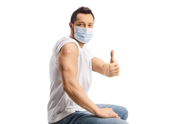 istock Young man with a mask showing his arm with a vaccine patch and gesturing thumbs up 1363987706
