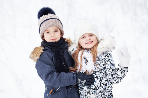 Portrait of beautiful cheerful children on white snow background. Pretty Models wearing winter jackets and hats