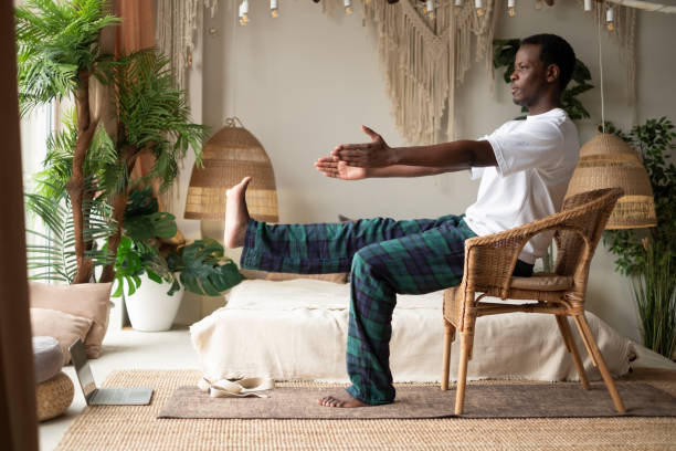African man using chair at his living room at home doing yoga asana for beginners. stock photo