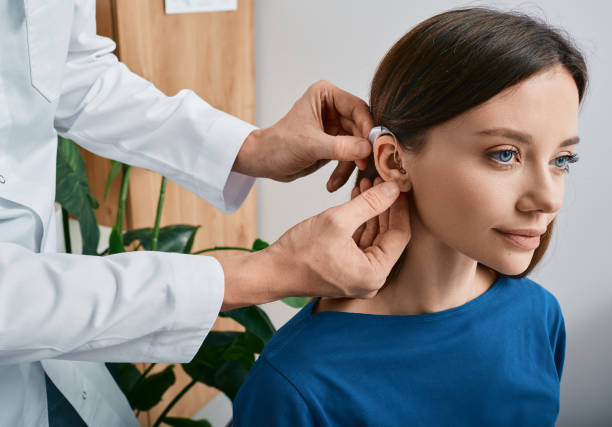 Installation hearing aid on woman's ear at hearing clinic, close-up, side view. Deafness treatment, hearing solutions stock photo
