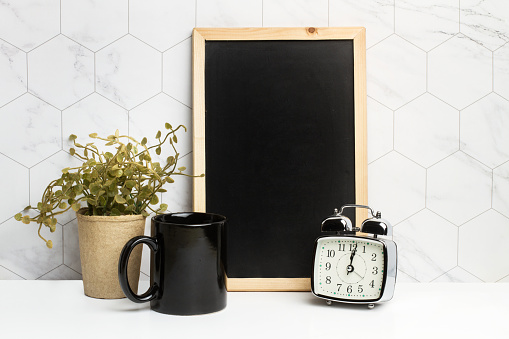 Black mug , blackboard and a bell alarm clock in front of a hexagonal tiled wall
