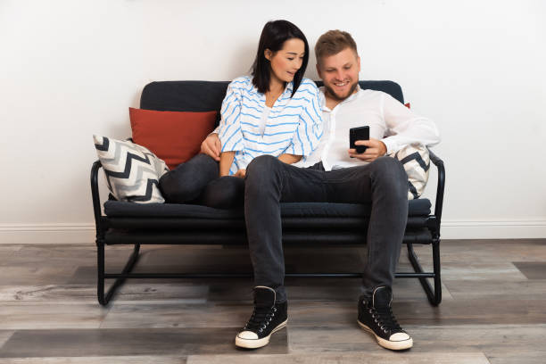 istock Loving couple man and woman sitting on sofa in apartment and smiling while using modern technics 1363997542