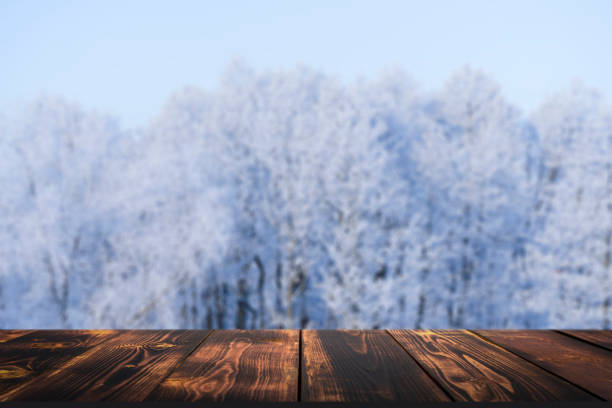 istock Winter forest with wooden table background. Blurred snow landscape and empty rustic table for product or merchandise. 1364000381