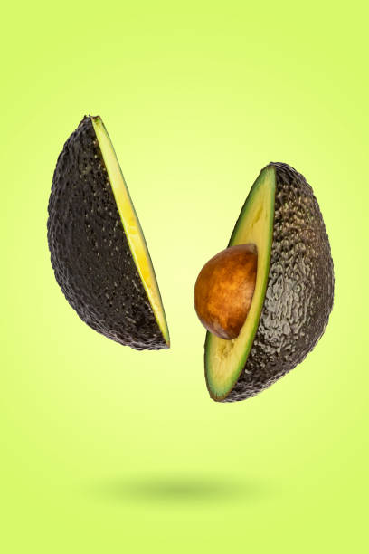 Ripe flying Avocado Hass halves on green background.