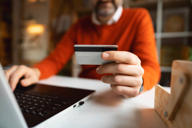 istock Unrecognizable man holdin credit card while online shopping from home office 1364005632