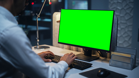 Close Up of a Businessman Working on Desktop Computer with Chroma Key Green Screen Mock Up Display. Male Executive Director Managing Digital Projects, Typing Data, Using Keyboard and Mouse.