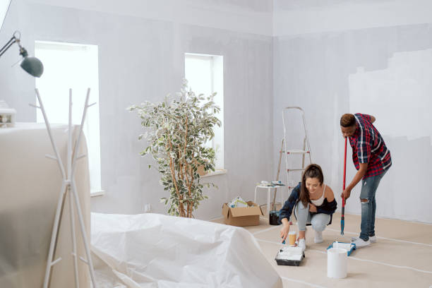 istock Two young cheerful people work together to finish apartment they hold paint rollers in hands they get dirty in white paint around them boxes ladder friends look into camera smile cooperate in painting 1364010004